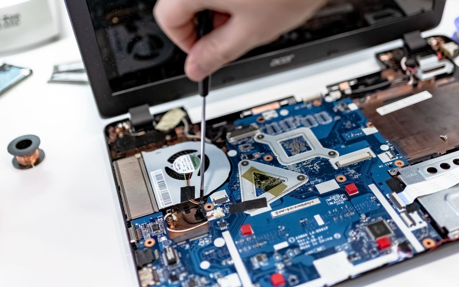 Hands using a precision screwdriver on the internal components of an opened laptop.